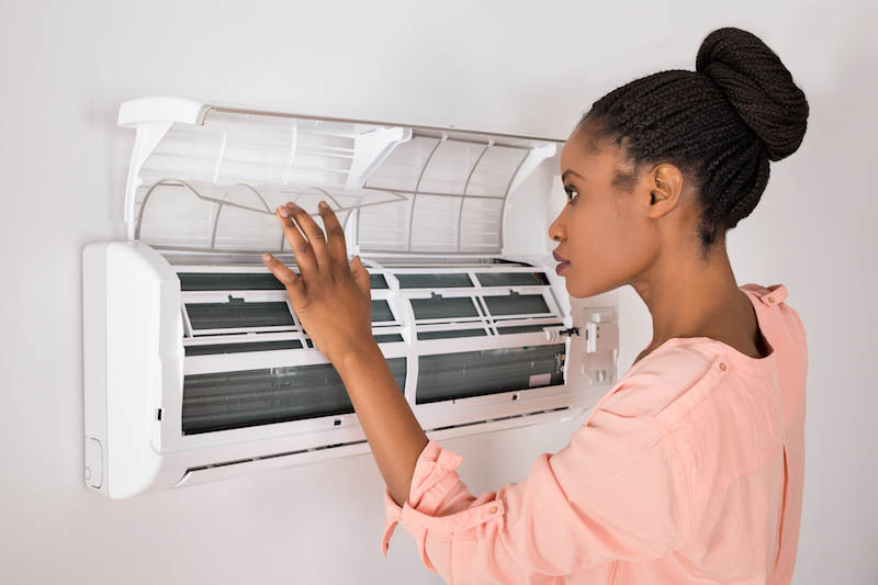 Young African Woman Opening Air Conditioner At Home