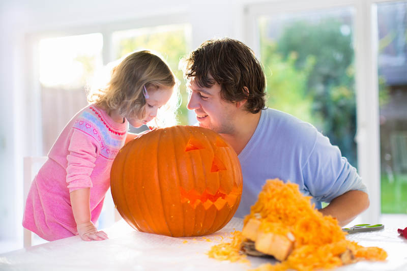 Family carving pumpkin at Halloween. Parents and children decorate the house. Kids and parents trick or treat. Father and child carve squash at home. Toddler kid with jack-o-lantern.